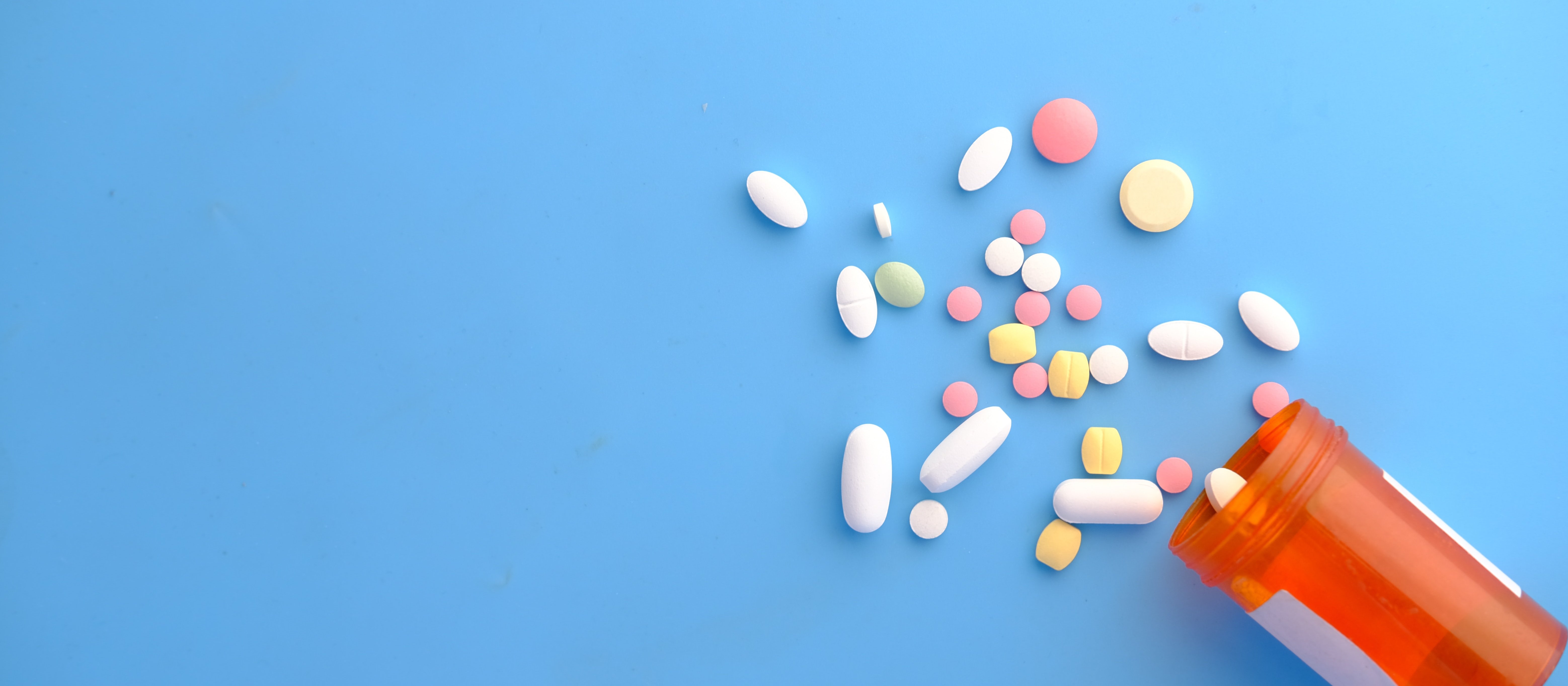 Different coloured pills spilling out of a medication jar on a blue background